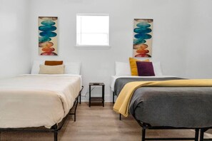 A hotel room with two beds, a small table, and artwork on the walls.