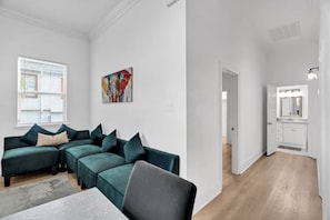 Una sala de estar moderna con un sofá modular, una mesa de comedor y una cocina visible a través de una puerta abierta.