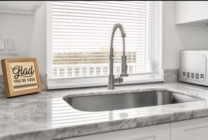 A kitchen with a stainless steel sink, a window with blinds, and a sign that reads "Glad you're here".