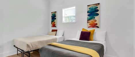 A bedroom with two beds, a ceiling fan, and abstract art on the walls.