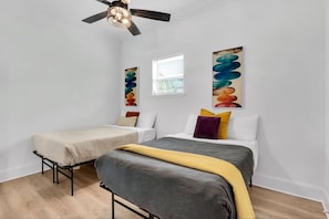Ein Schlafzimmer mit zwei Betten, einem Deckenventilator und abstrakter Kunst an den Wänden.