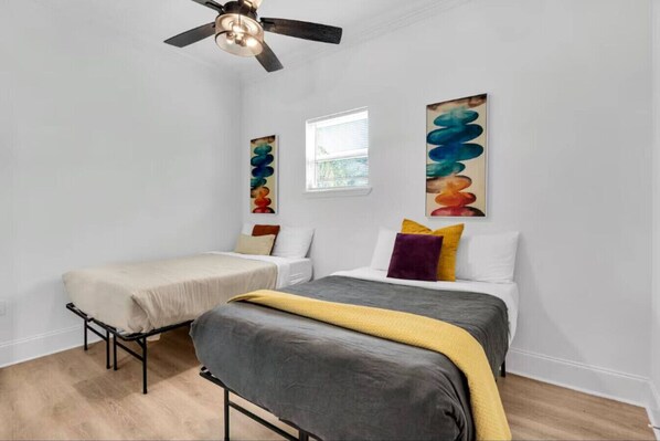 A bedroom with two beds, a ceiling fan, and abstract art on the walls.