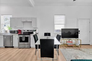 A modern kitchen with white cabinets, a stainless steel oven, and a dining area with a table and chairs.