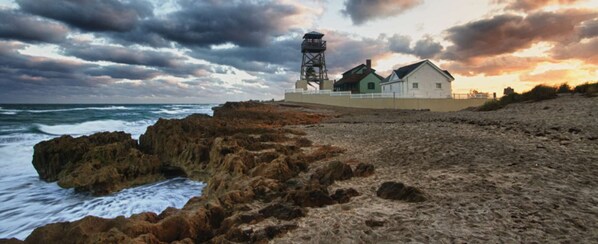 A coastal building with a lighthouse, a beach, and rocky terrain.