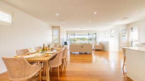 A spacious, modern kitchen with a dining area, wooden flooring, and large windows offering a view of the outdoors.