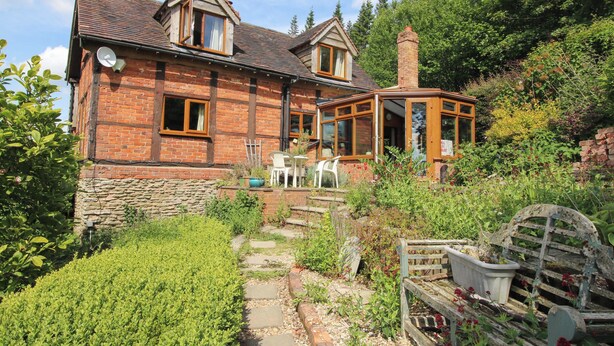 Une maison en briques avec un jardin, un chemin de pierres et un banc en bois.