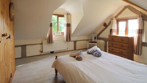 Une chambre avec un plafond en pente, un lit avec une literie à rayures, une commode en bois, une chaise et une fenêtre avec des rideaux.