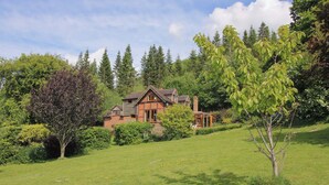 Une grande maison à la façade en pierre, entourée d’un paysage verdoyant et luxuriant et de grands arbres.