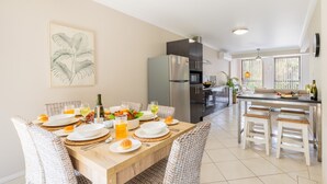 Une cuisine moderne avec un coin repas, comprenant un grand îlot central, des appareils en acier inoxydable et une vue sur l’extérieur.