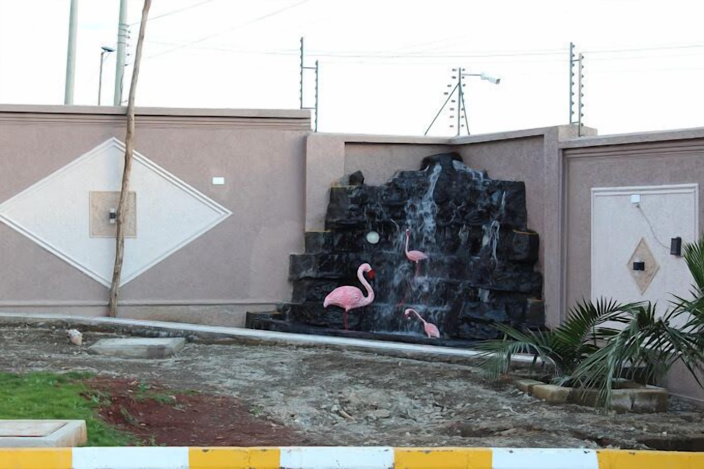 Una fuente de agua con cascada y flamencos, rodeada por una zona de hormigón con un borde amarillo y blanco.