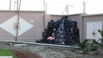 Una fuente de agua con cascada y flamencos, rodeada por una zona de hormigón con un borde amarillo y blanco.