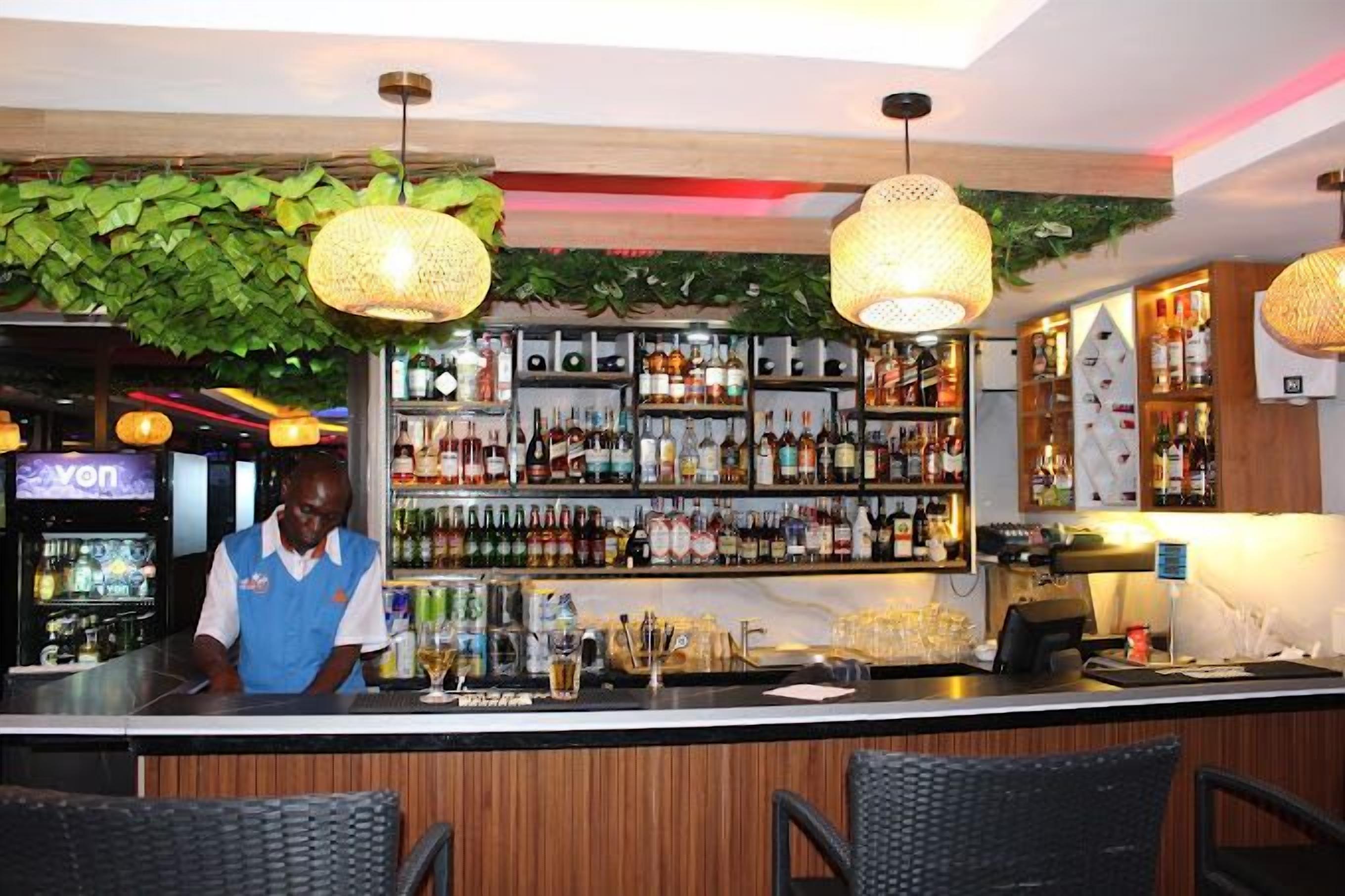 Eine Bar mit Bartender, Flaschenregalen, hängenden Korblampen und einem 'von'-Schild im Hintergrund.