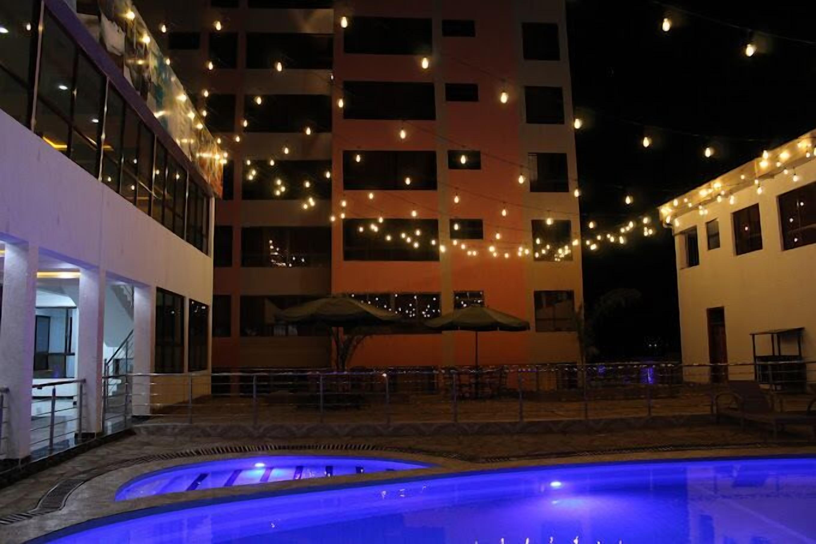 An outdoor pool area with string lights, a building with multiple windows, and a covered seating area.