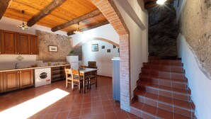 A kitchen with wooden cabinets, a washing machine, and a dining area with a table and chairs. - CASALE GELSi APT. GELSI(AMALFI COAST) (Campania)