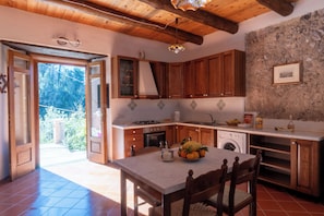 Una cocina con armarios de madera, encimera de mármol, un fregadero, una estufa y una mesa de comedor con sillas.