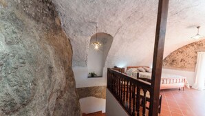 Ein rustikaler Innenraum aus Stein mit einer Holztreppe, einem Bett und einer Hängelampe.