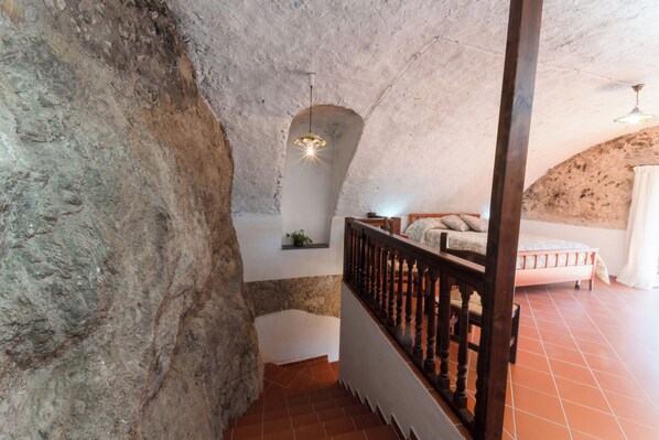A rustic interior with a stone wall, a wooden staircase, a bed, and a hanging light fixture.