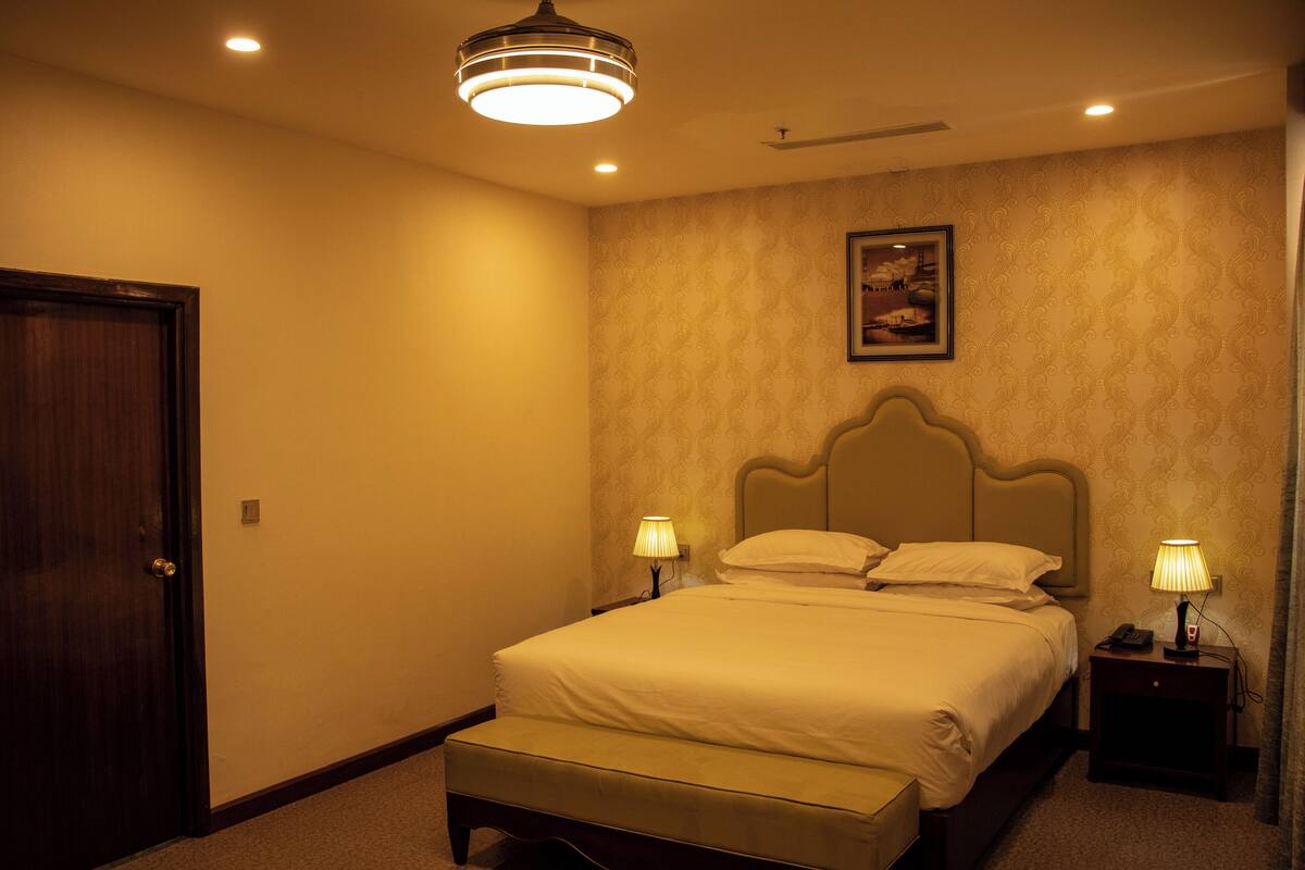 A hotel room with a bed, bedside lamps, a nightstand, a framed picture on the wall, and a door.