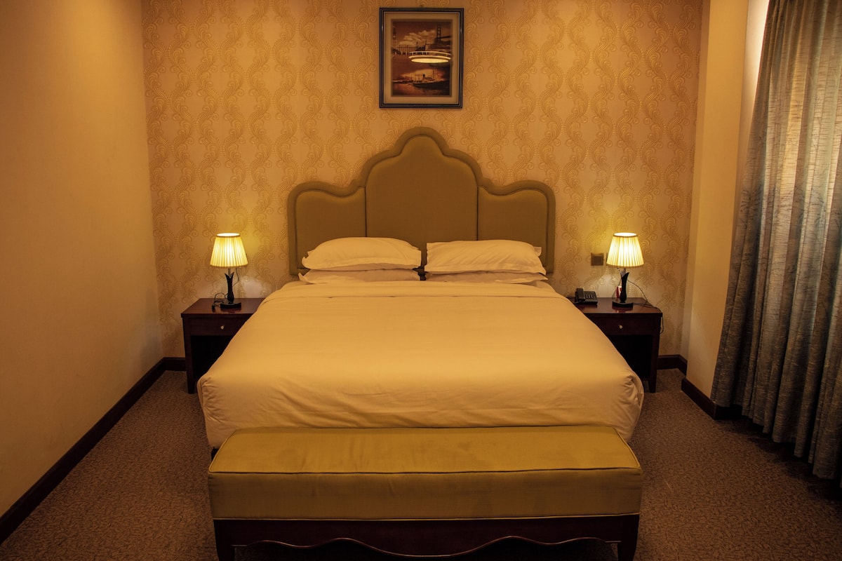 A neatly made bed with a headboard, two bedside lamps, and a framed picture on the wall.