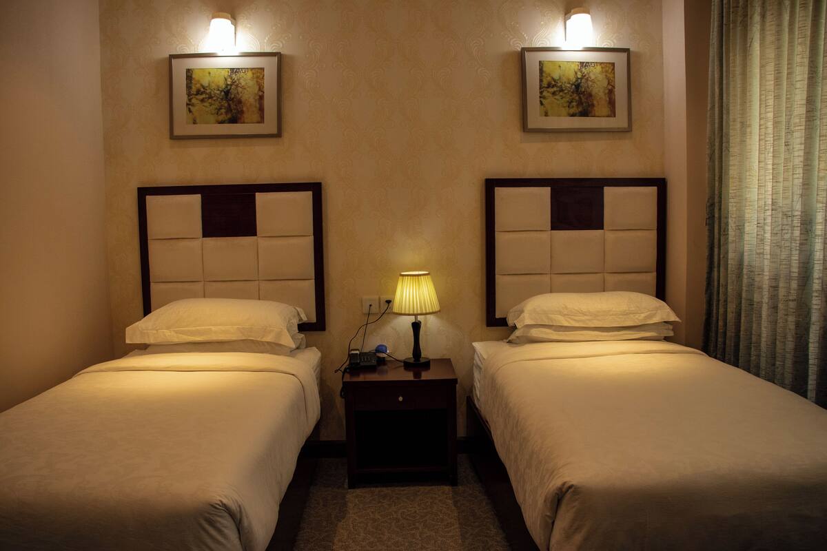 A hotel room with two beds, each with a headboard, a nightstand with a lamp, and framed artwork on the wall.
