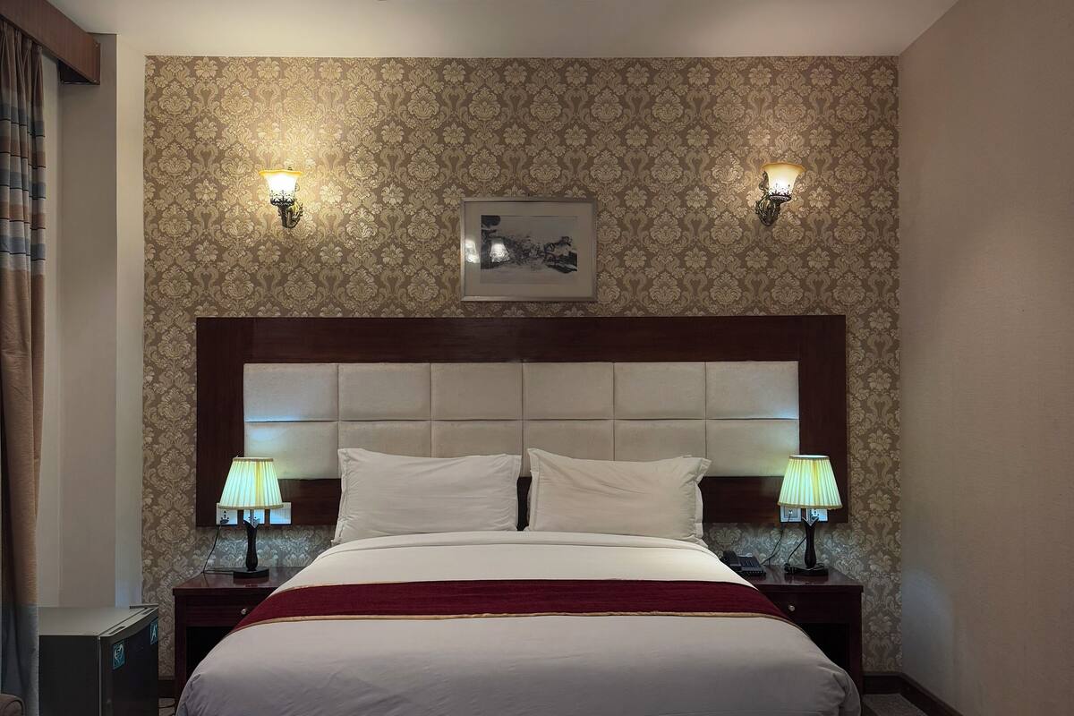 A hotel room with a large bed, two bedside lamps, a ceiling fan, and a framed picture on the wall.