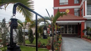A hotel entrance with a red facade, a tiled roof, and a garden with potted plants and a pathway leading to the entrance. - RATNA HOTEL (Biratnagar)