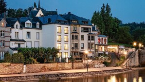 A riverside hotel with multiple stories, a prominent sign, and a stone wall along the water. - Vacation Home in Bouillon by Semois River (Bouillon)