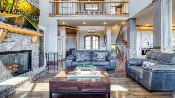 A spacious living room with a stone fireplace, leather sofas, and a large painting of a forest.