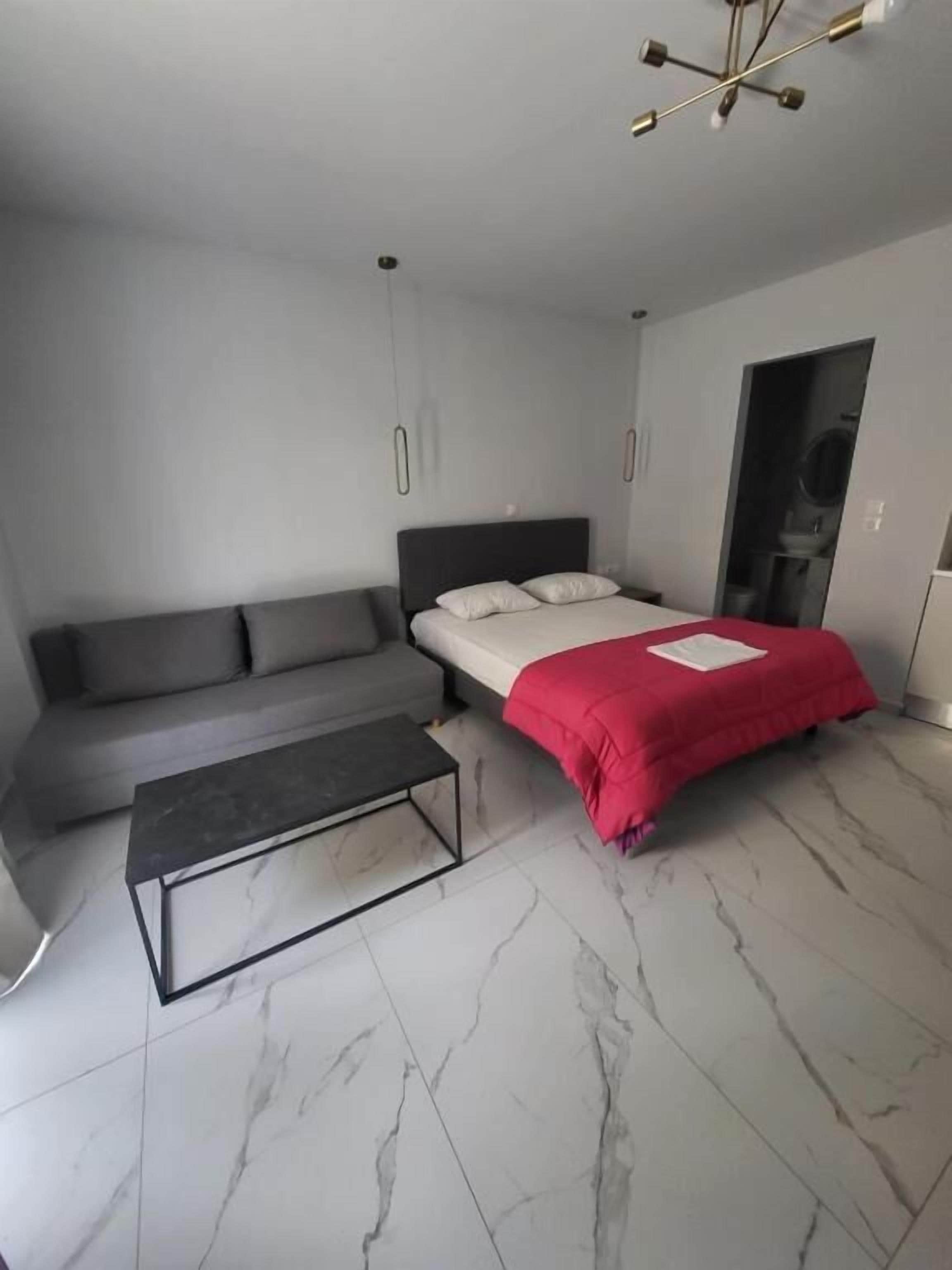 Un dormitorio moderno con un sofá gris, una cama con una manta roja y un suelo de mármol.