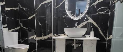 A modern bathroom with a marble backsplash, a round mirror, a white sink, and a toilet.