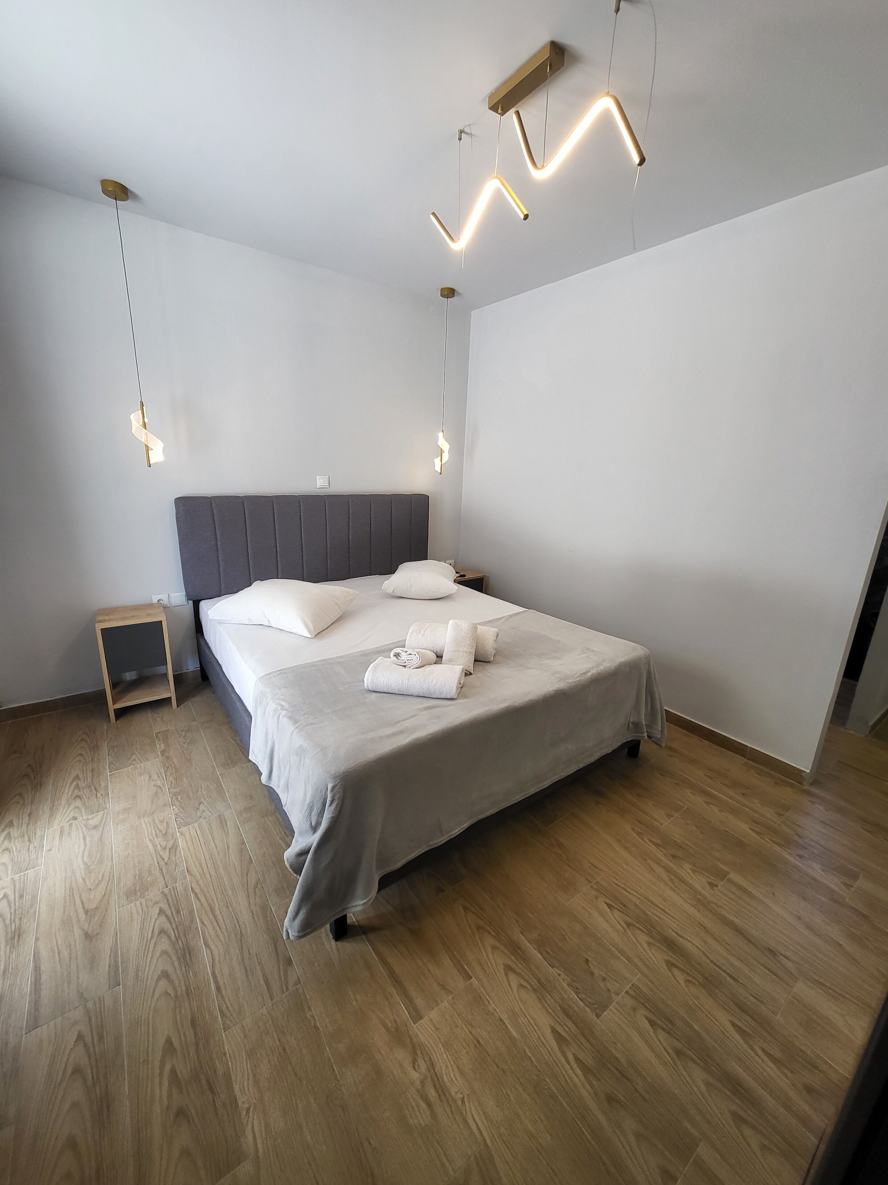 A modern bedroom with a large bed, a bedside table, and a hanging light fixture.
