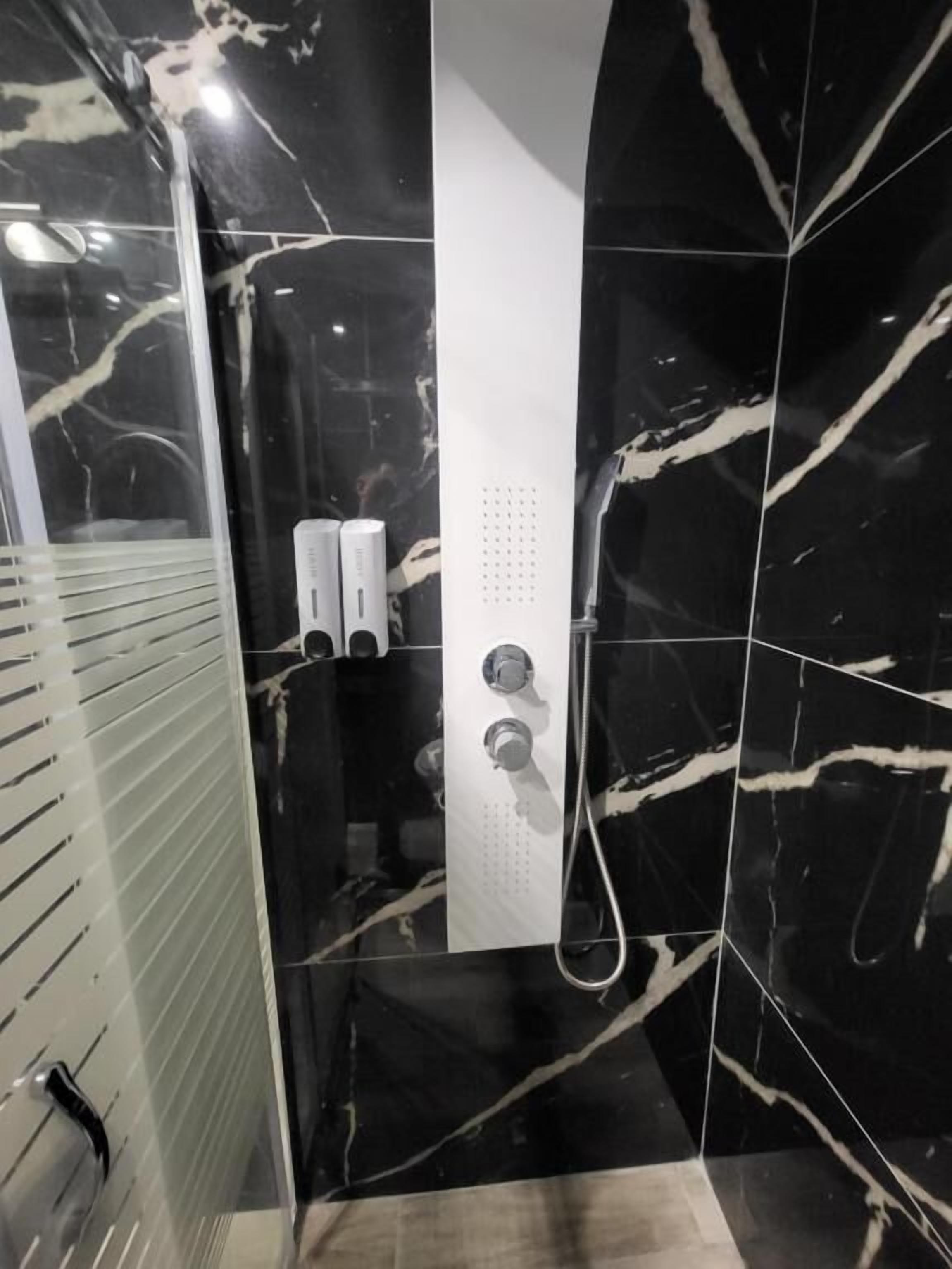 Ein modernes Badezimmer mit schwarzen Marmorfliesen, einer Duschkabine aus Glas und einer weißen Bedienkonsole.