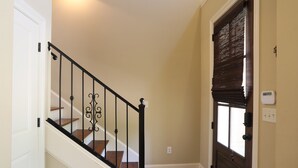 Un escalier avec une rampe noire, une porte en bois dotée d’une fenêtre et un interrupteur sur le mur.
