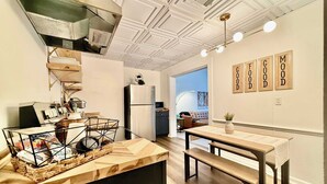 A modern kitchen with a built-in stove, a dining area with a wooden table and bench, and a view of a living room with a sofa and a lamp. - Off Street Reserved Parking, Full Kitchen, Newly Renovated (Verona)
