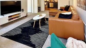A modern living room with a TV, sofa, coffee table, and kitchen in the background. - Off Street Reserved Parking, Full Kitchen, Newly Renovated (Verona)