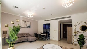 A modern living room with a sectional sofa, dining table, and chairs, a small coffee table, and decorative plants. - Spacious 1BR with Balcony in JLT (Dubai)