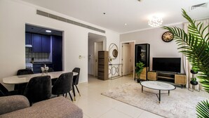 A modern living room with a dining area, a TV, and a kitchen visible through an open door. - Spacious 1BR with Balcony in JLT (Dubai)