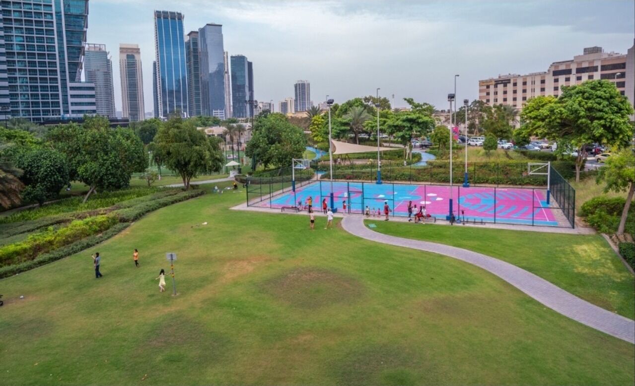 An outdoor basketball court surrounded by greenery and city buildings.