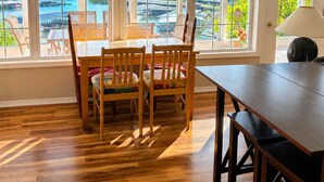 A dining area with a view of a body of water and buildings, wooden flooring, and a table with chairs. - Lakefront 4BD/2.5BA Grill/Dock/Sleeps 13PP (Osage Beach)
