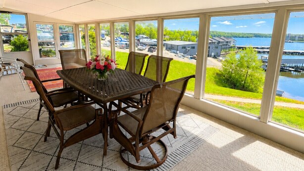 A covered patio with a table and chairs, large windows, and a view of a body of water and buildings. - Lakefront 4BD/2.5BA Grill/Dock/Sleeps 13PP (Osage Beach)