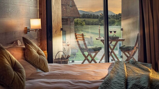 A bedroom with a large window, wooden headboard, and a view of a countryside landscape. - Agriturismo Villa di Modolo (Belluno)