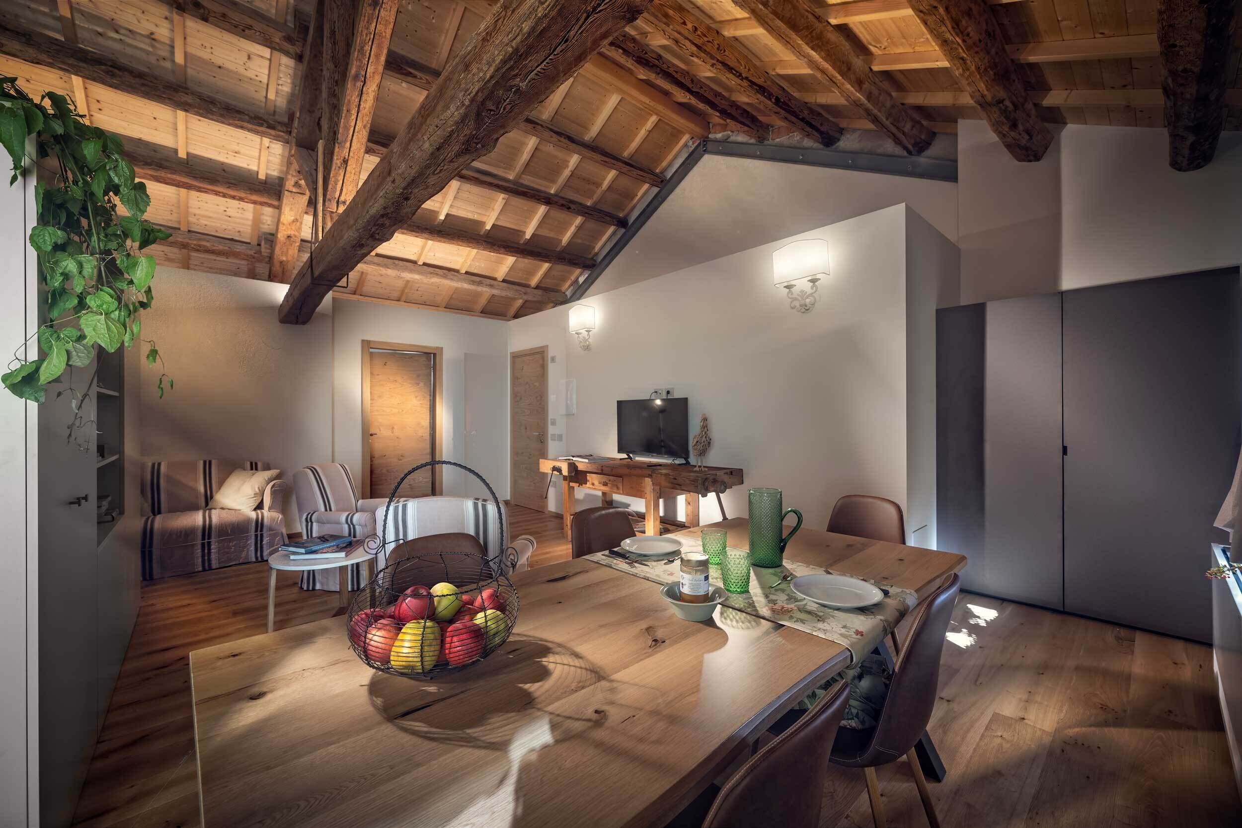 Un vaste espace de vie doté d’un plafond en bois, d’une table à manger avec des chaises, d’un canapé et d’un téléviseur en arrière-plan.