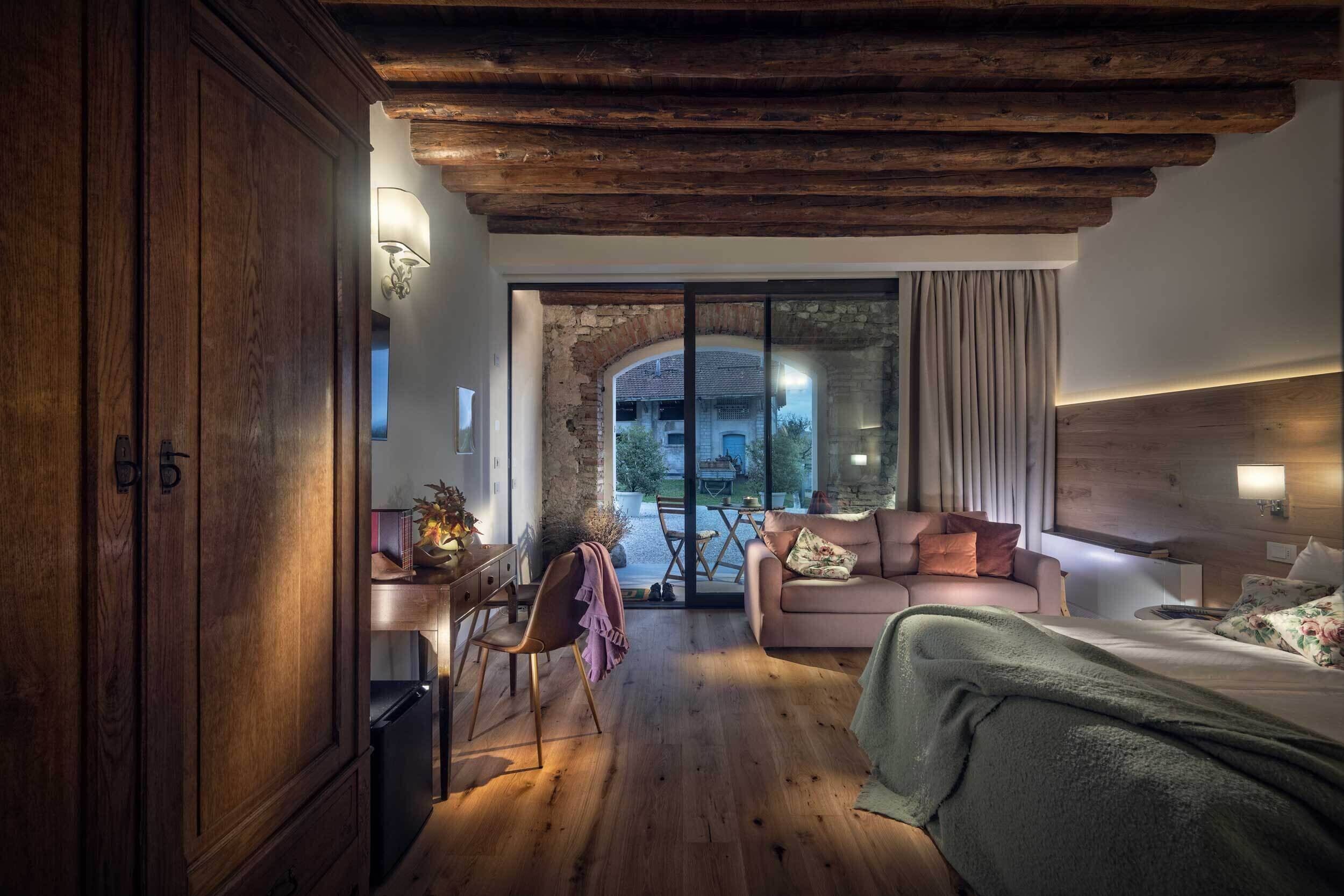 Una habitación de hotel acogedora con techo de madera, una cama, un sofá, un escritorio y vistas a un área exterior a través de un ventanal.