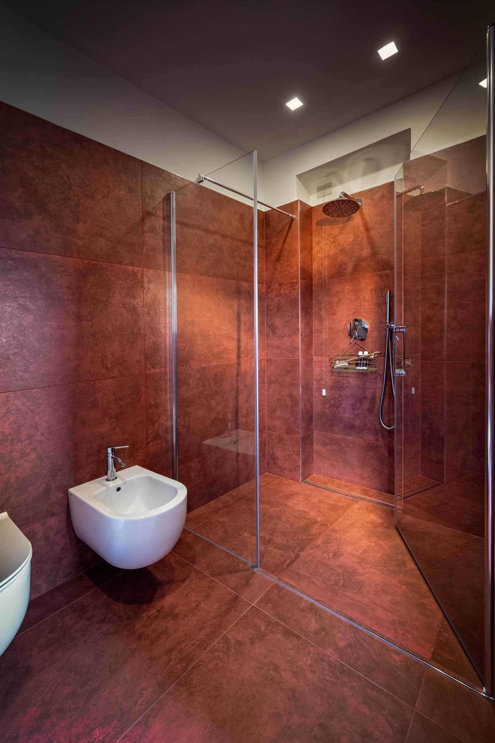 A modern bathroom with a glass-enclosed shower, a white pedestal sink, and a marble accent wall.