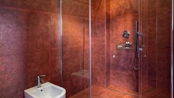 A modern bathroom with a glass-enclosed shower, a white pedestal sink, and a marble accent wall.