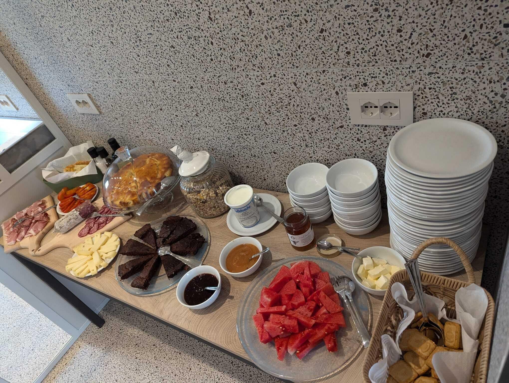 A buffet table with various food items, including meats, cheeses, and fruits, along with serving dishes and utensils.