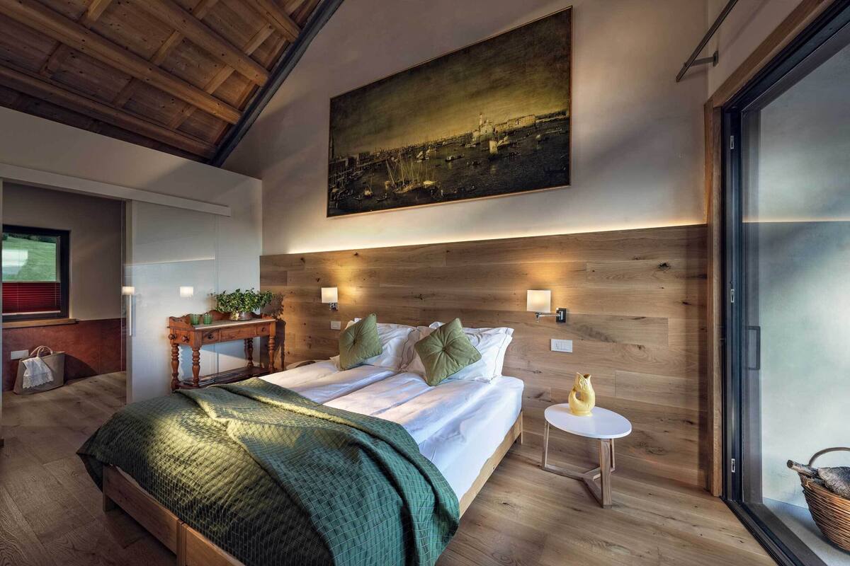 A modern bedroom with a large bed, wooden headboard, and a cityscape painting above.