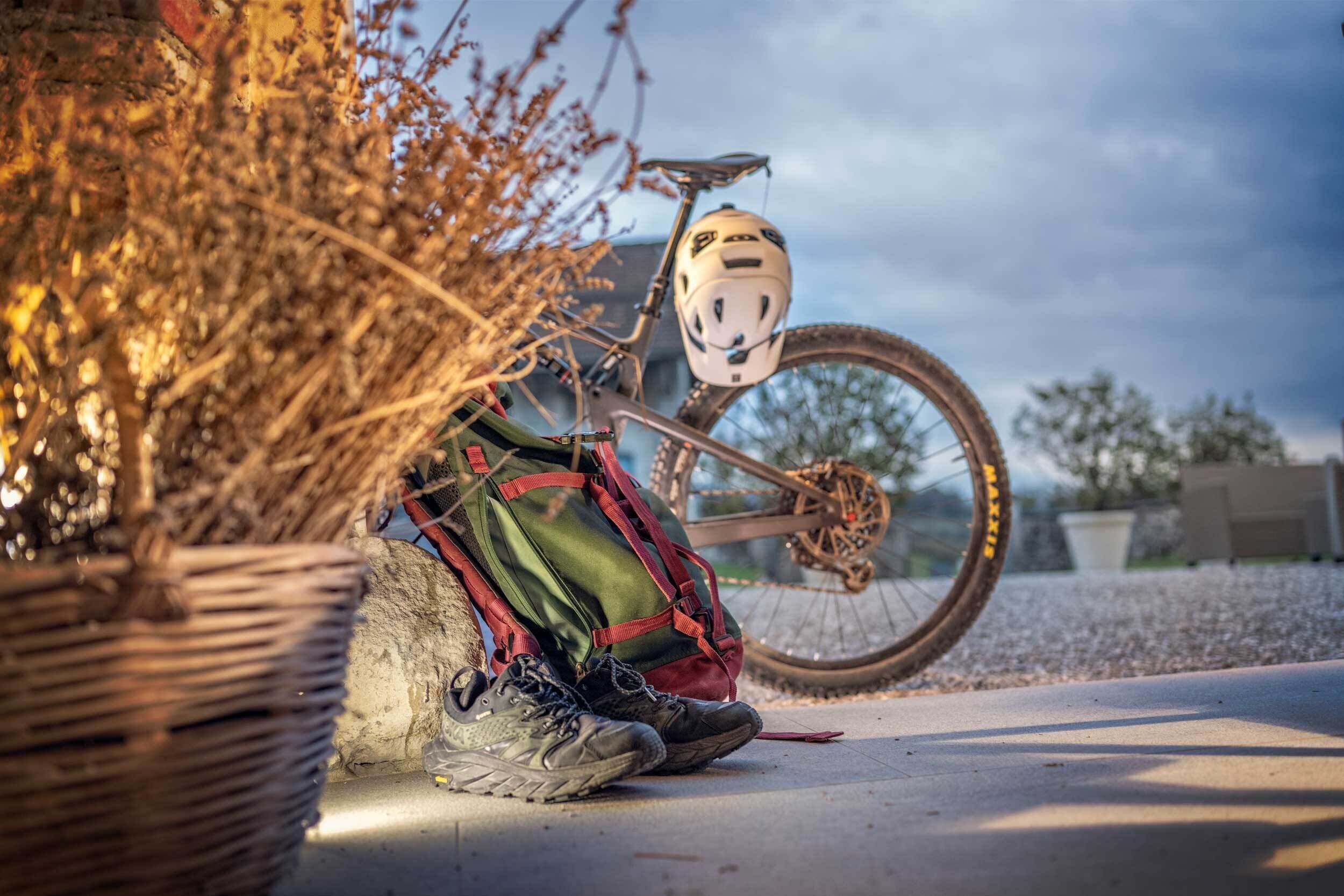 Una bicicleta con casco y una mochila verde apoyada en una pared.