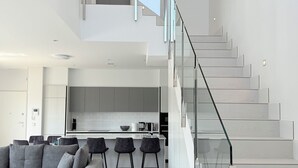 A modern interior with a staircase, a living area with a sofa and chairs, and a kitchen area.