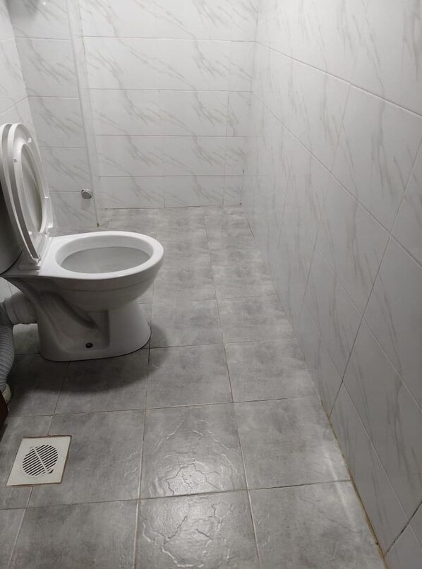 Un baño con inodoro, zona de ducha y suelo de baldosas.